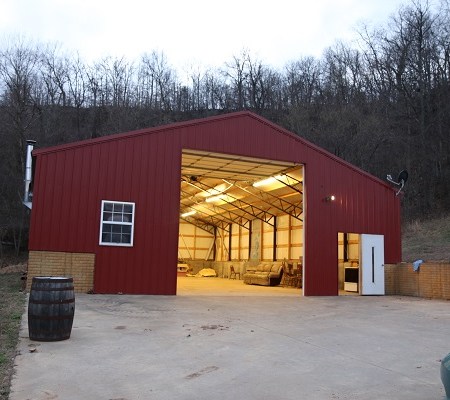 The red metal building at dusk with its large door open and lights on inside