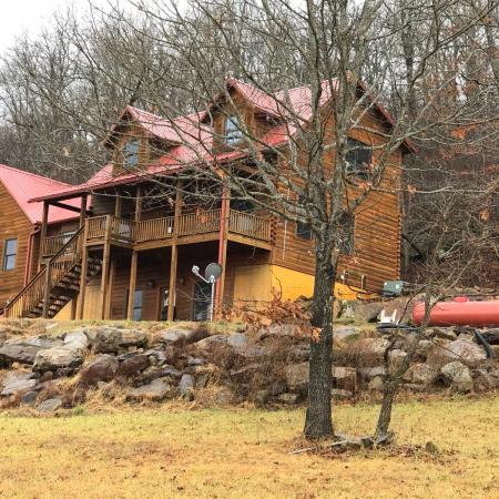 The Living Springs Log House in winter with a red metal roof, deck, and rock wall