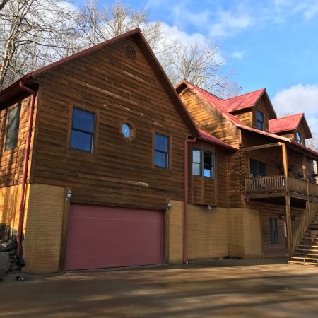 The Living Springs Log House from the driveway, with garage door, windows, and stairs up to the deck