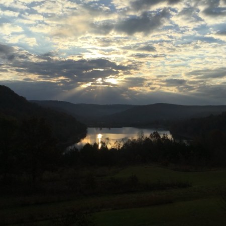 Sun breaking through clouds over a dark ridge and a lake at dusk