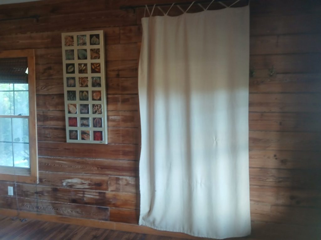Long cream curtain drawn over a window on the cypress wall of the master bedroom, beside a leaf art print