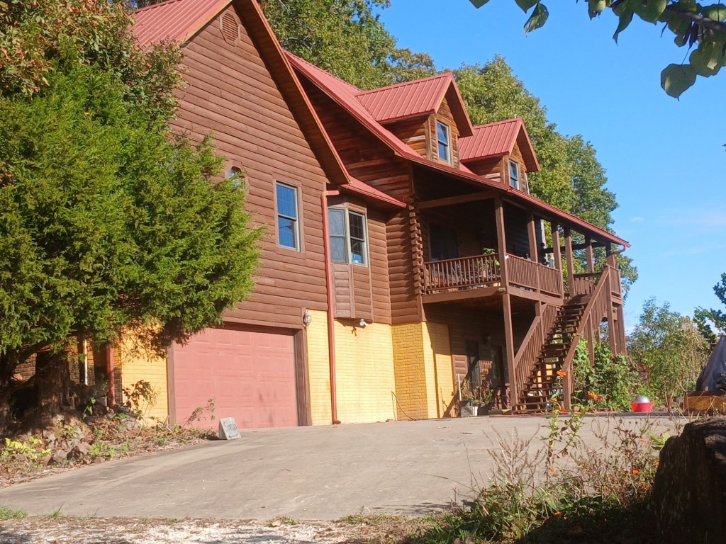 Side view of the Living Springs Log House from the paved driveway, showing the garage, the walk-out lower level, and the outside stairs up to the deck