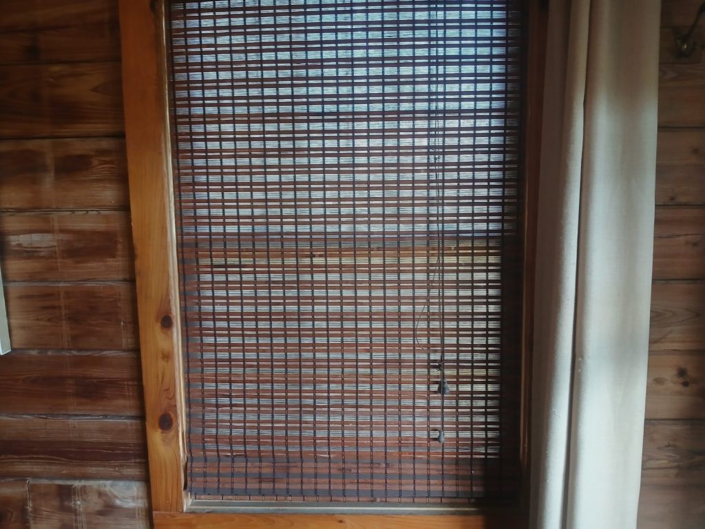 Bamboo shade pulled down over a bedroom window, framed by cypress walls